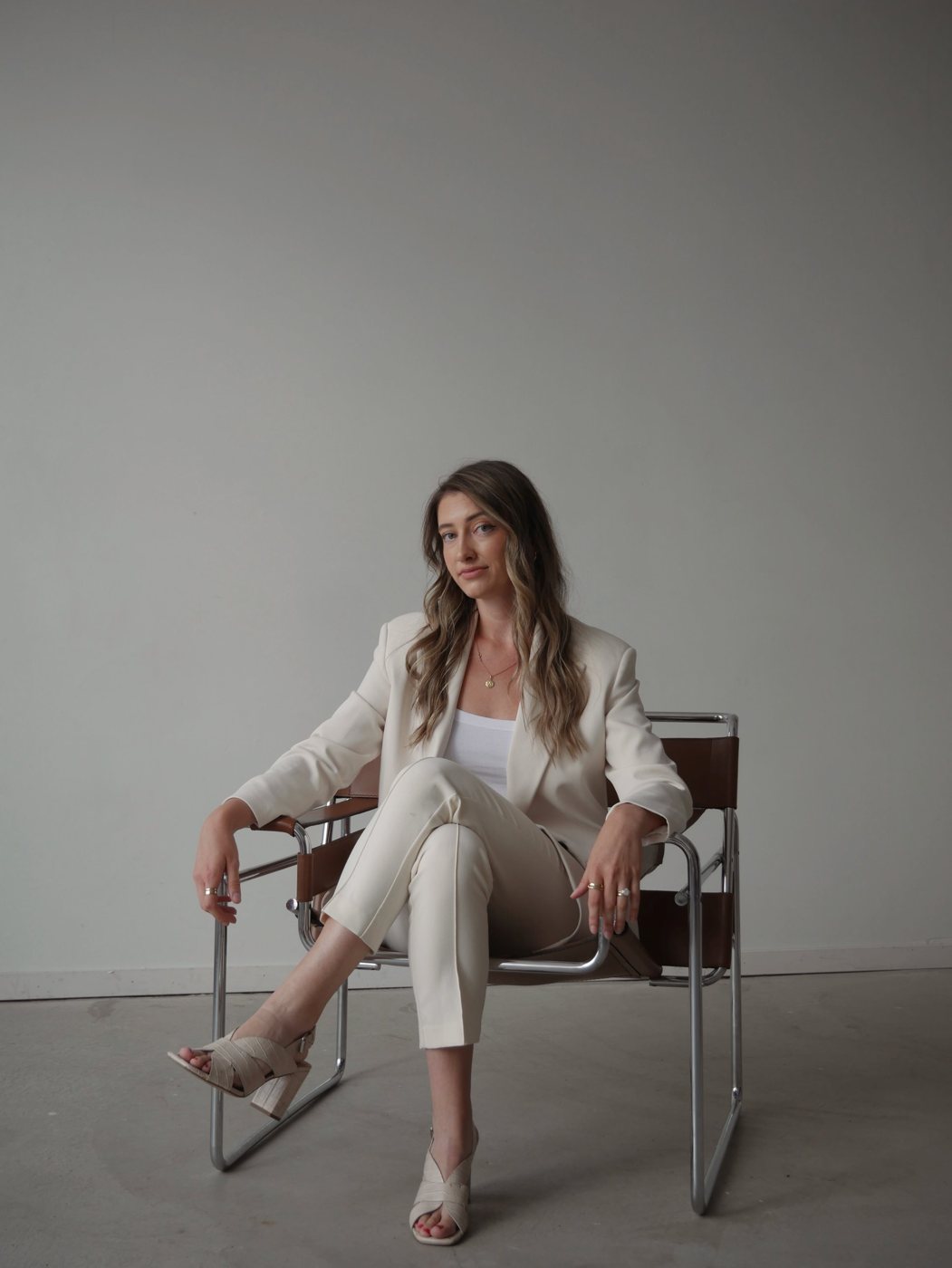Hailey Piper in a cream suit, seated in a leather and chrome chair